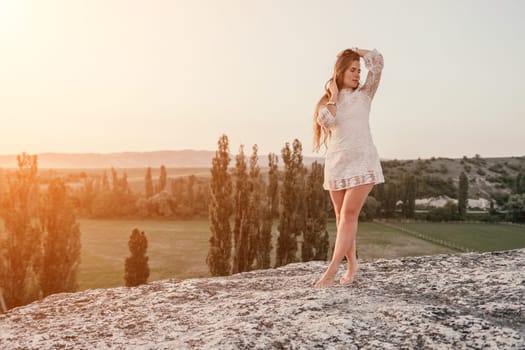 Romantic beautiful bride in white dress posing with sea and mountains in background. Stylish bride standing back on beautiful landscape of sea and mountains on sunset