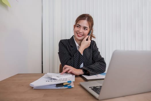 Asian businesswoman in a formal suit in the office is happy and cheerful while using a smartphone to work in her office..