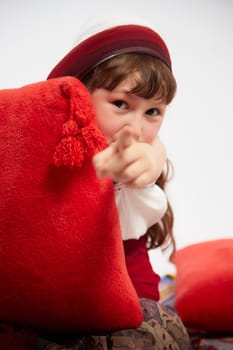 Portrait of Little girl in a stylized Tatar national costume having rest with a red pillow on a white background in the studio. Photo shoot of funny young teenager who is not a professional model