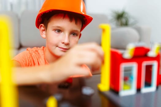 Child boy in helmet playing and building with colorful plastic bricks at the table.