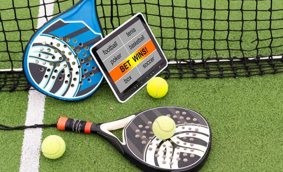 Yellow balls on grass turf near padel tennis racket behind net in green court outdoors with natural lighting. Paddle is a racquet game. Professional sport concept with copy space. High quality photo