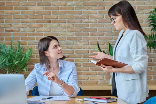 Two businesswomen talking and discussing in office. Female colleagues, manager and employee analyze and discuss documents, contracts, financial reports. Work law finance teamwork people job concept