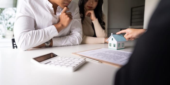 Young married couple sitting at table listening to realtor, real estate agent, loan broker or mortgage advisor telling about options.