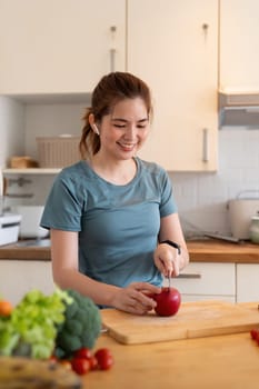 Woman asian cutting fruits and vegetable to prepare a smoothie while listening to music with earphones in the kitchen at home.