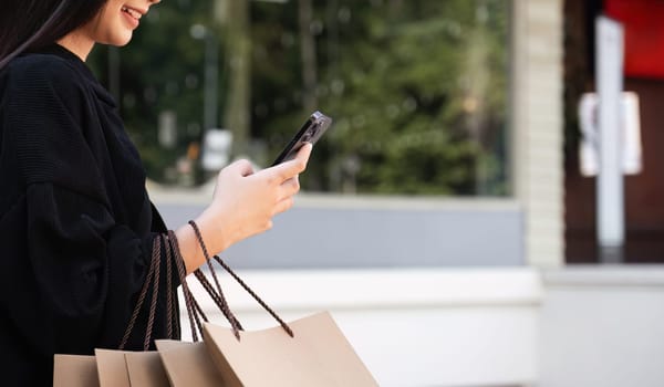 Asian woman using smartphone and looking away while enjoying a day shopping. Black Friday sale and discount. Buying clothes presents for holidays.
