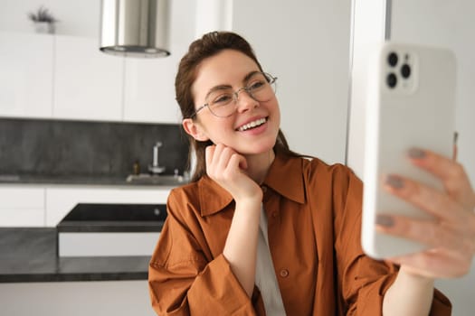Happy smiling woman in glasses, taking selfie, recording video on smartphone, video chats on mobile phone application.