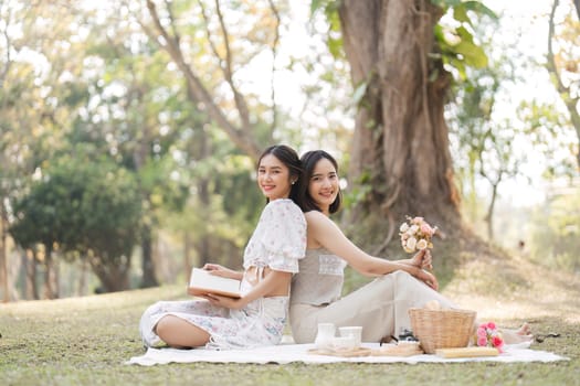 Two beautiful LGBT young women in casual clothes and summer hats Carefree woman having a picnic outside Positive model sitting on the grass eat fruit and cheese Take a selfie. LGBT concept.