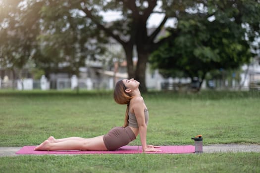 Young healthy Asian woman stretch her body on a yoga mat. Do yoga in a lush park Yoga and Pilates concept.