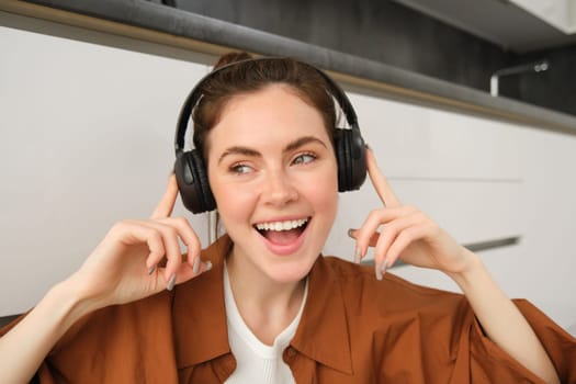 Carefree female model in wireless headphones, listens to music, enjoys favourite tunes in earphones, sings along and smiles.