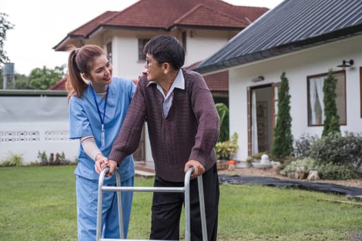 Asian female caregiver helps senior man walk A senior using a walker is assisted by a nurse at home. A nurse helps an elderly patient at a nursing home. Elderly care and healthy lifestyle.