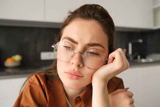 Close up portrait of woman in glasses with concerned, sad face, looking upset, troubled expression, sitting at home.