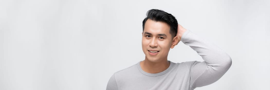 Positive young asian male looking away with smile while standing against white background