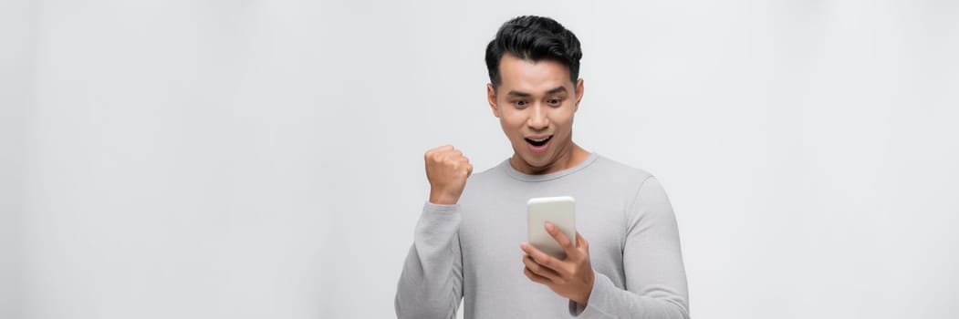 Excited asian man isolated on  white background look at smartphone happy get good text message