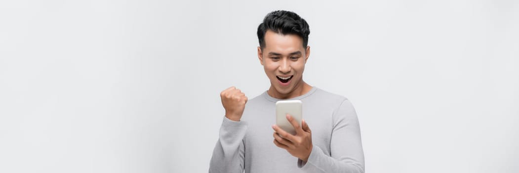 Excited asian man isolated look at smartphone happy win lottery on mobile app online