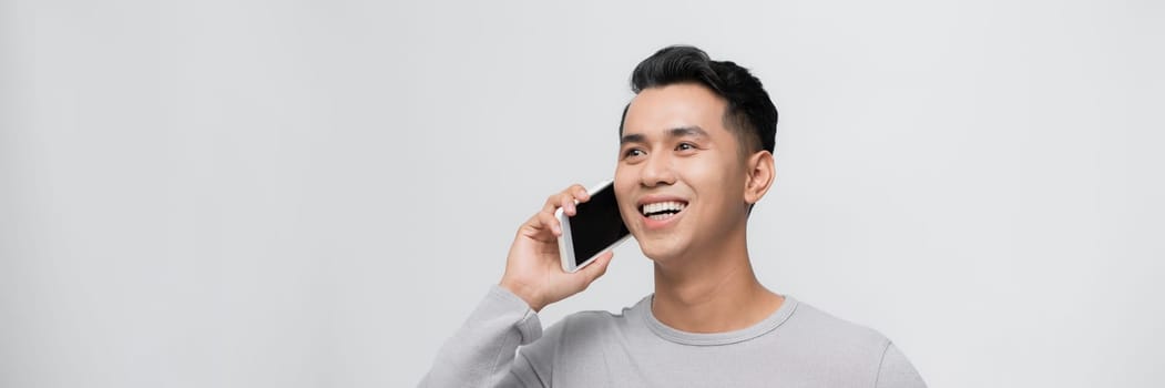 Handsome young man talking on smartphone against grey background.