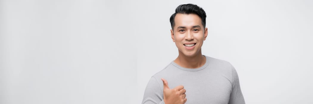 Young handsome asian man over white banner background doing happy thumbs up gesture with hand.