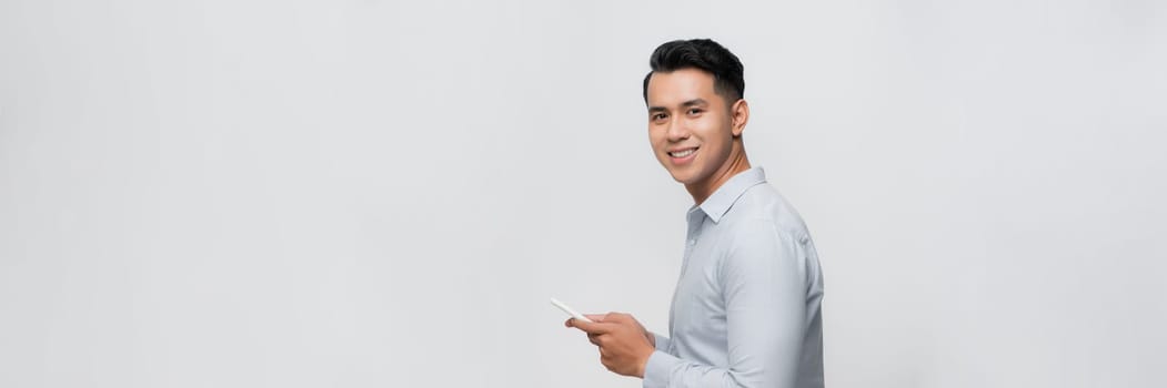 Handsome young man using his phone with smile while standing against white background.