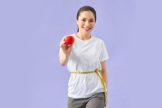 woman measuring waist with tape on knot isolated on violet background, holding red apple