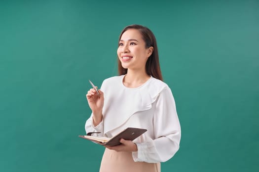 Young business woman standing enjoy using a pen writing diary note book on green background.