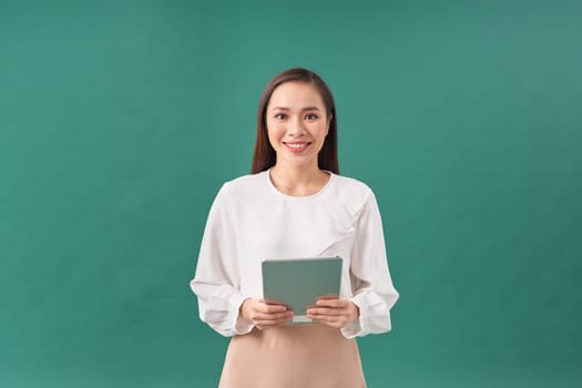 Smiling attractive businesswoman wearing formal wear holding tablet device on green background