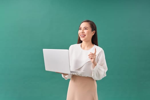 cheerful young woman standing isolated over green background using laptop computer
