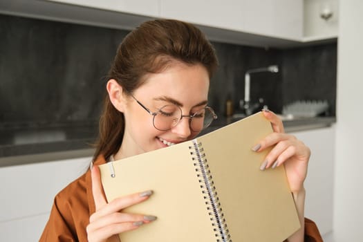 Portrait of beautiful woman in glasses, college girl smiling, sitting in kitchen with notebook.