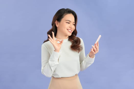 Portrait of asian woman showing OK sign and using mobile phone, recommend application