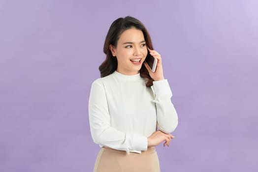 A smiling young asian woman talking on mobile phone isolated over pastel color background