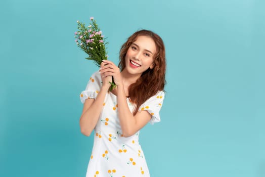 A beautiful young asian woman posing isolated over blue background holding flowers.