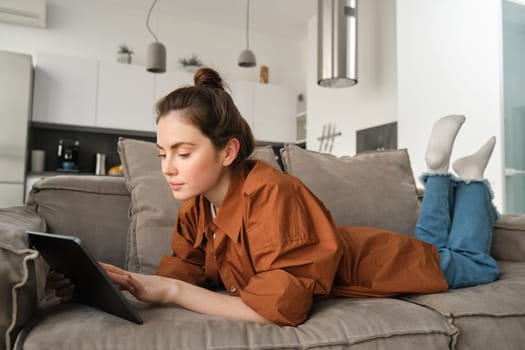 Weekend and lifestyle concept. Young woman lying on couch with digital tablet, scrolling social media, reading e-book or watching tv series on app.