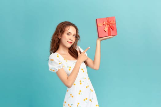 Portrait of a smiling young woman in summer dress holding gift box isolated over blue background