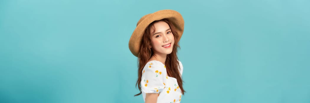 Beautiful smiling young woman in summer straw hat isolated on pastel blue background. 