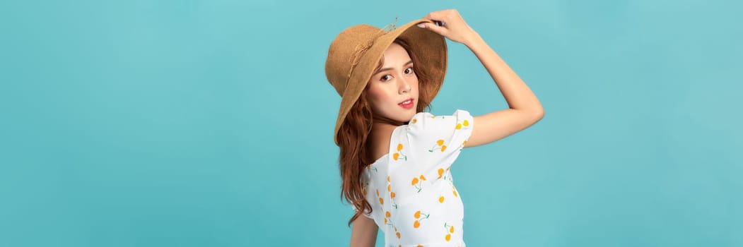 Cheerful young asian woman in summer dress and straw hat isolated on blue background.