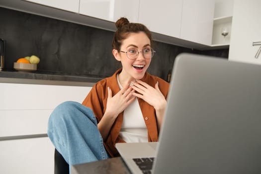 Work from home, remote job concept. Young woman sitting in kitchen, using laptop, joins video chat conversation, give online lessons, talking to client on computer.