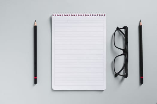 Top view of empty notebook, glasses and pen on grey office desk