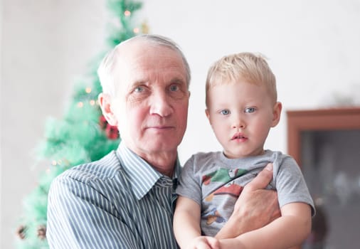 portrait of grandfather holds his grandson in his arms and both laugh, the Christmas tree,continuity of generations, raising children, sweet home, High quality photo
