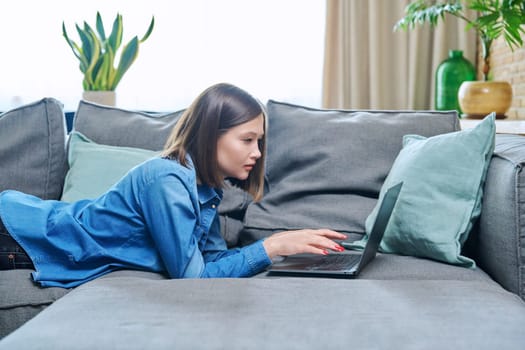 Young woman lying on sofa using laptop. Internet technologies for study leisure, female freelancer working remotely, university student watching online course, rest communication in social networks