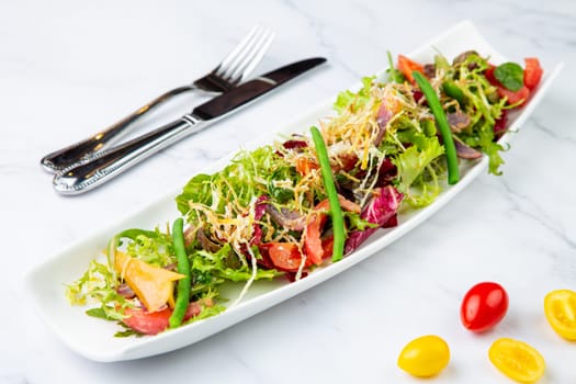 green salad with cherry tomatoes on a white oblong plate