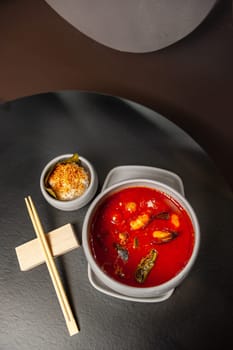 Tom Yum Kung spicy Thai soup with shrimp in a grey bowl on a dark stone background, top view, copy space. High quality photo