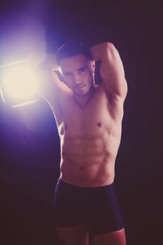 Confident, attractive shirtless muscular young man topless in a studio