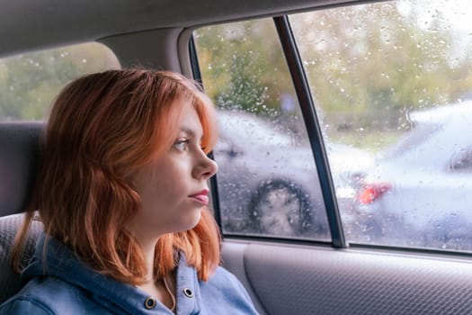 A pretty girl with pink hair relaxed in the back seat of a car, looking out the window, she is immersed in thoughts about her future, about opportunities. Travel and transportation