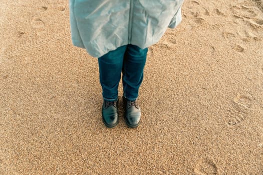 a girl walks on an autumn deserted beach. women's feet in brown leather boots on the sand of an autumn beach.