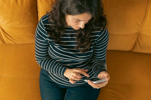 a relaxed woman on a home sofa with her smartphone on a social network. active life position. The girl is typing a text message. view from above