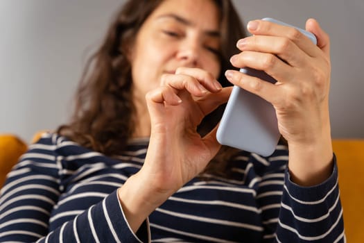 a relaxed woman on a home sofa with her smartphone on a social network. active life position. The girl is typing a text message. view from above