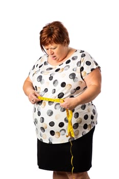 Overweight fifty something woman, measuring her waist with a yellow measuring tape, isolated on a white background