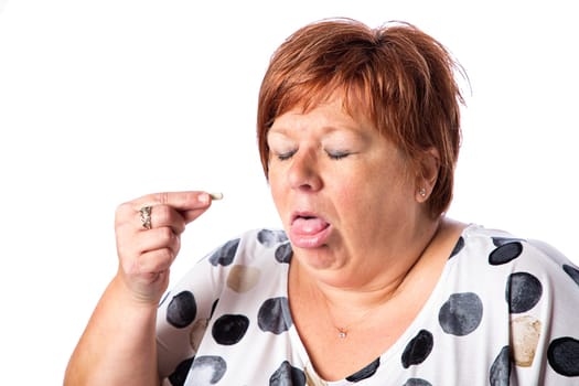 Overweight fifty something woman, making a disgusted face trying to swallow a pill, isolated on a white background