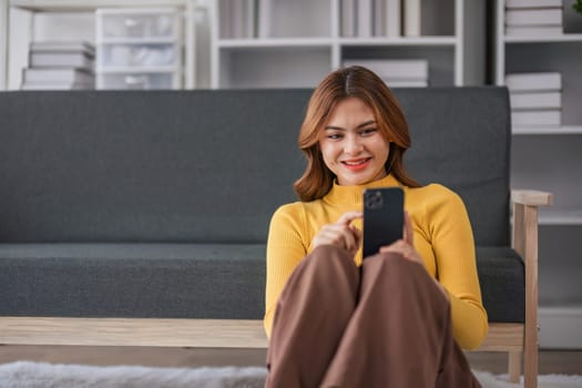 Happy Asian woman playing with mobile phone while sitting on sofa at home Young woman smiling relaxedly with headphones in the morning It's time to rest..