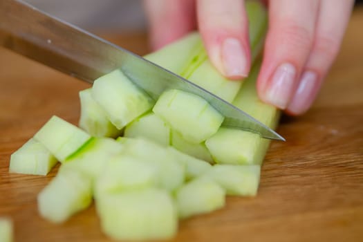 A woman's hands cut a green cucumber into small slices, close-up. Long green cucumber slices are suitable for salads or as a side dish. Preparing cucumbers for salad. High quality photo