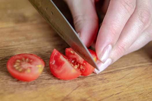 A hand cuts a cherry tomato with a knife close-up. Preparing salad to set the table. High quality photo