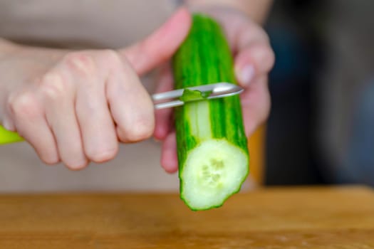 Close-up of a woman's hand peeling a cucumber. Peeling cucumber skins for salads or just to eat. High quality photo. High quality photo